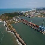 Vista aérea do Porto de Imbituba, em Santa Catarina, com docas, guindastes, navios e contêineres.