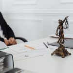 Mesa de trabalho com uma estátua da Justiça, documentos jurídicos e um laptop.