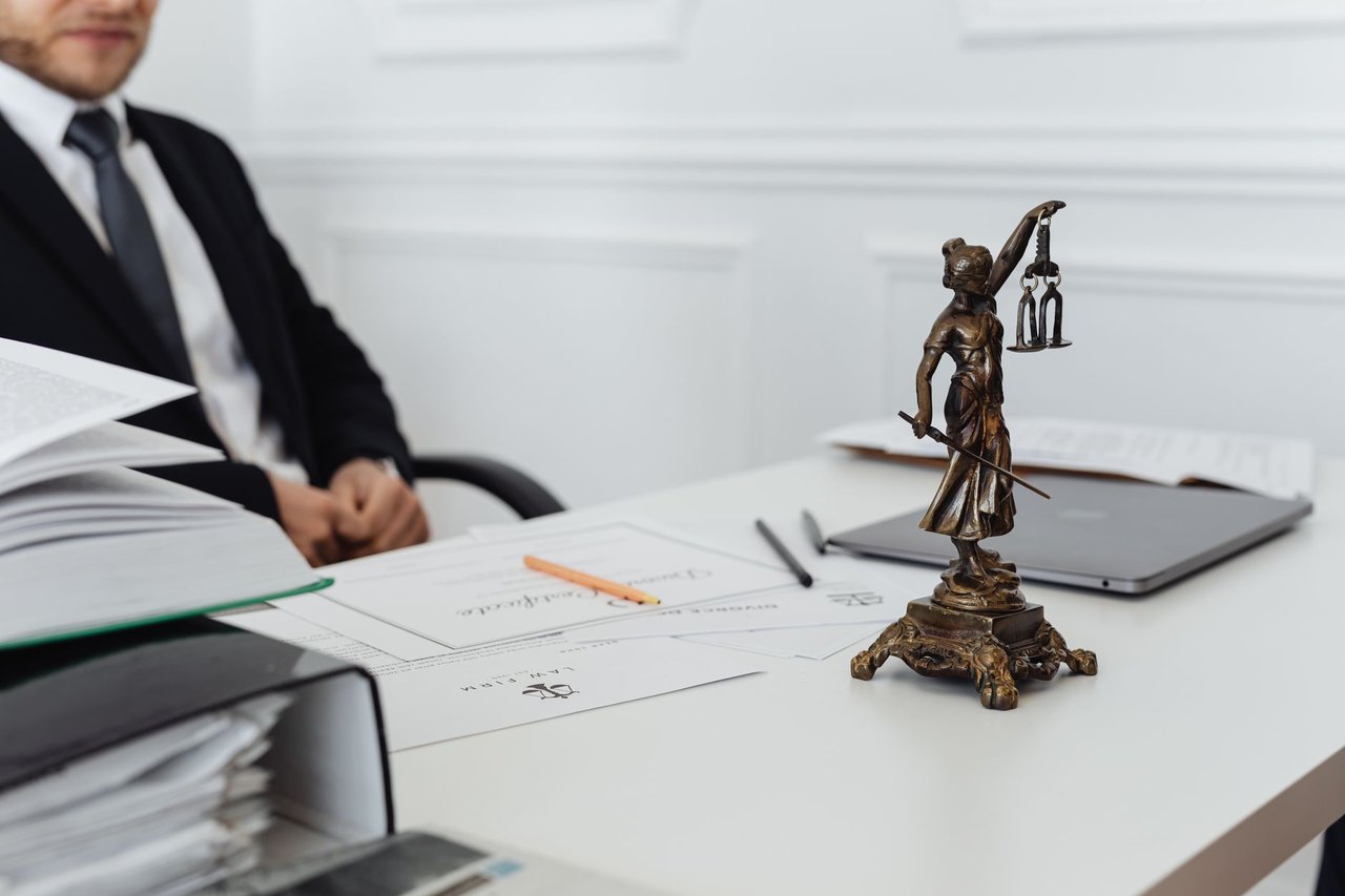 Mesa de trabalho com uma estátua da Justiça, documentos jurídicos e um laptop.