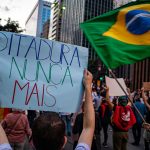 Manifestantes participam de ato em São Paulo, carregando cartazes sobre direitos humanos e democracia.