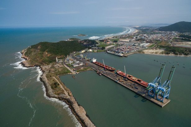 Vista aérea do Porto de Imbituba, em Santa Catarina, com docas, guindastes, navios e contêineres.