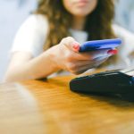 Mulher aproxima um smartphone de um terminal para realizar um pagamento digital.