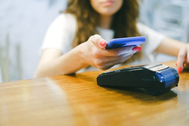 Mulher aproxima um smartphone de um terminal para realizar um pagamento digital.